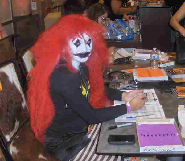 Red-wigged female clown sits at checkin for ScareLA