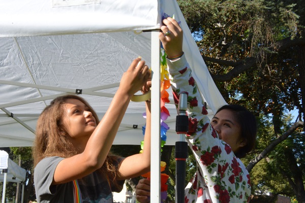 volunteers hang a rainbow garland on the preformance tent
