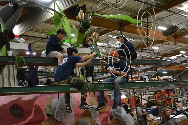 Three young men sit on a green girder above a float to add dry materials