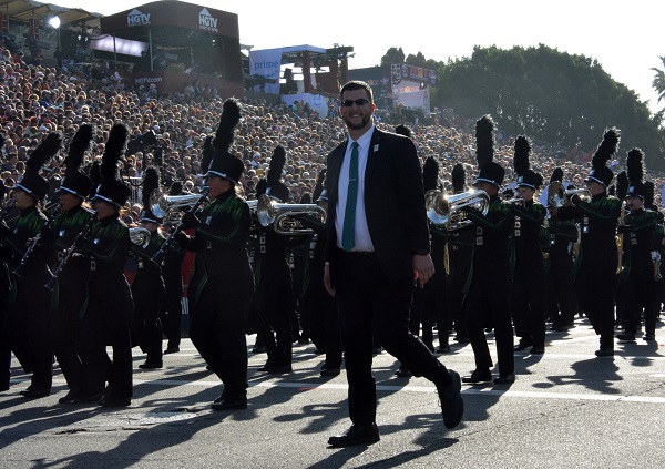 Homestead High band director in black suit with a green tie marches with his musicians in 129th Rose Parade