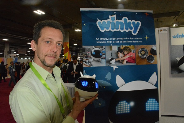 Nicolas George stands near Winky robot signa nd holds robot in Eureka Park Marketplace area of CES 2018