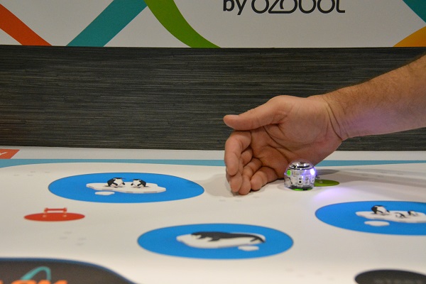 hand blocks one-inch Ozobot robot from painted blue lake on game board