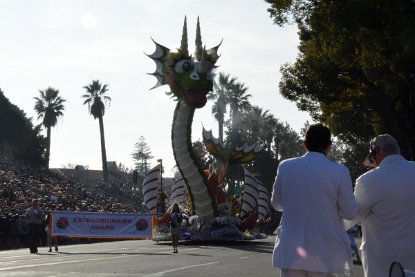 Sea monster float with "Extraordinaire" award banner appraches TV Corner as two White Suiters watch