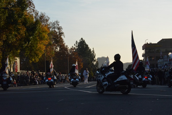 Motorcycle police with American flag and Rose Parade flags ride onto Colorado Boulevard