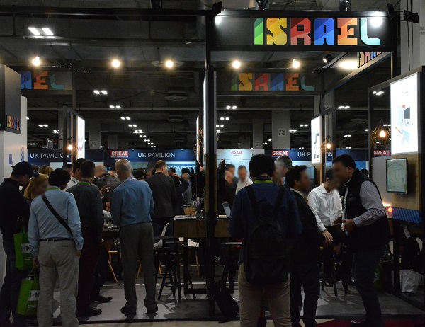 Group of men in business suits around the "ISRAEL" sign at Eureka Park Marketplace, with UK section in the background