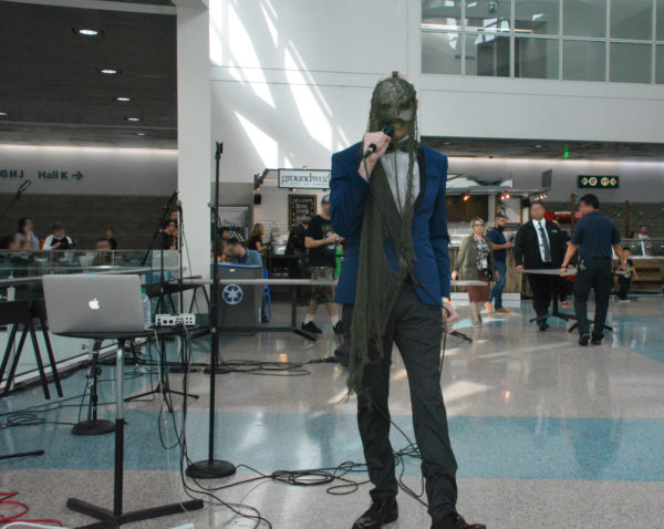 Musician Ban Sidh, in a green mask, singing outside entrance of ScareLA 2018 as attendees await admission