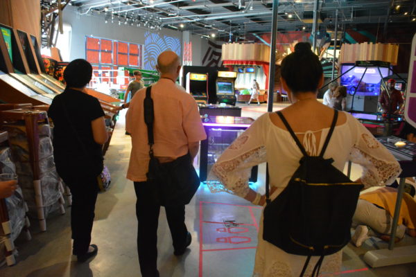 Three visitors walk into the Micro Amusement ParkRobot designer Daniel Busby with robotic bartender "Gearmo Del Pouro" at Micro Amusement Park™ arcade