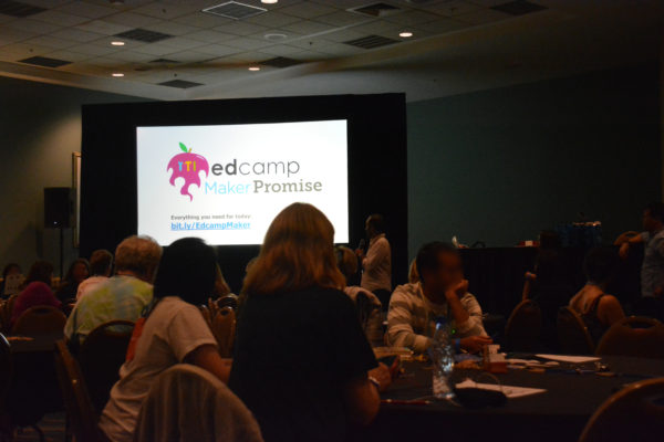 Teachers around tables back in the main room with Edcamp slide in front of the room