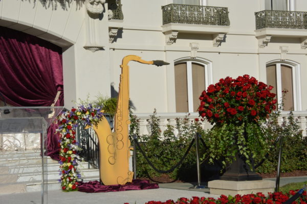 Saxophone cutout overflows with flower garland near a purple curtain at Tournament House Grand Marshal announcement