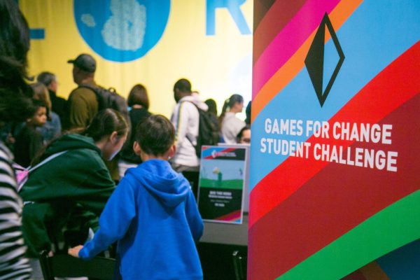 Sudents working next to their computers near sign that says, "Games For Change Student Challenge"