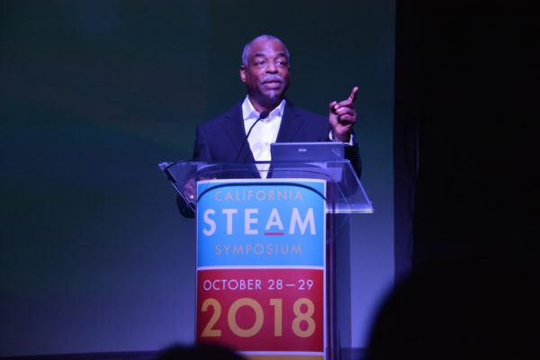 LeVar Burton raises his index finger as he speaks from California STEAM Symposium podium