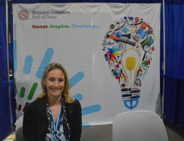 Blonde woman exhibitor smiles from National Inventors' Hall of Fame table at California STEAM Symposium 2018