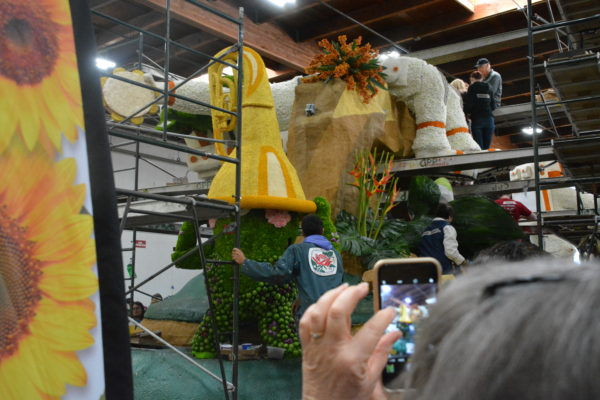 Green "alien" made with button carnations and green tomatillos with his head stuck in a gold trumpet on Cal Poly's Rose Parade® float