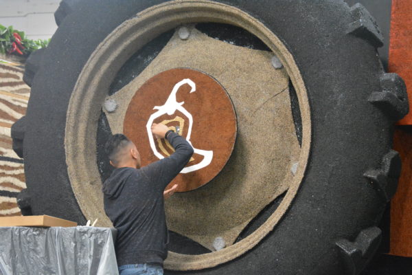 Volunteer adds detail to pepper symbol on wheels of the "tractor" on Chipotle Rose Parade® float