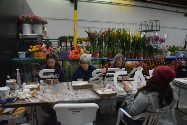 Volunteers glue plant materials to white letters spelling out "Cal Poly Universities"