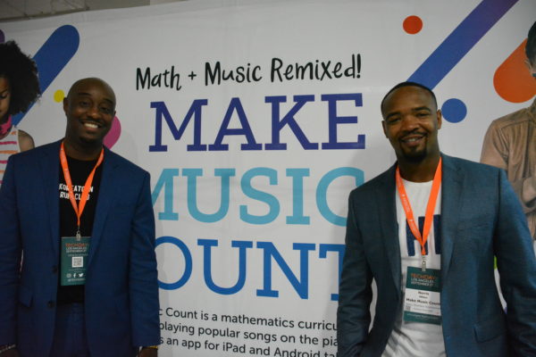 Marcus Blackwell, Jr. poses with associate in front of Make Music Count sign