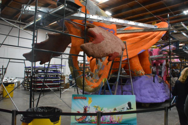 Orange winged "Dragon" Rose Parade® float behind scaffolding