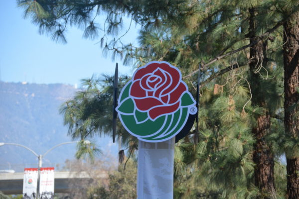 Rose Parade® emblem outside "Decorating Places" location with mountains and trees in the background 