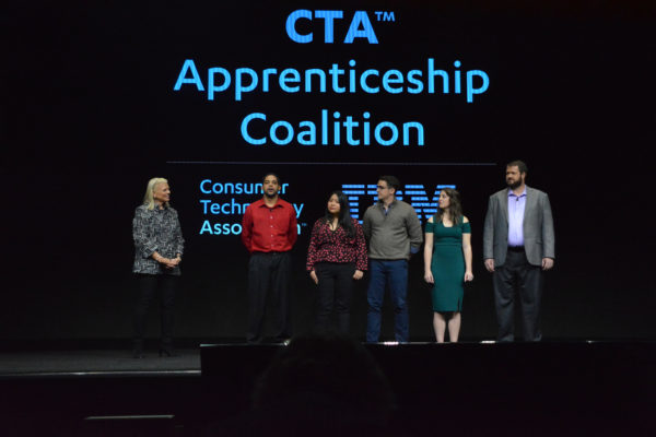 Ginni Rometty stands onstage with five members of apprenticeship program under slide reading, "CTA Apprenticeship Coalition"