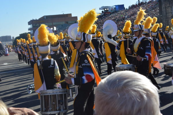 Drummer in navy band uniform with white hat and gold plume plays facing audience directly as column before her heads away at a 45-degree angle