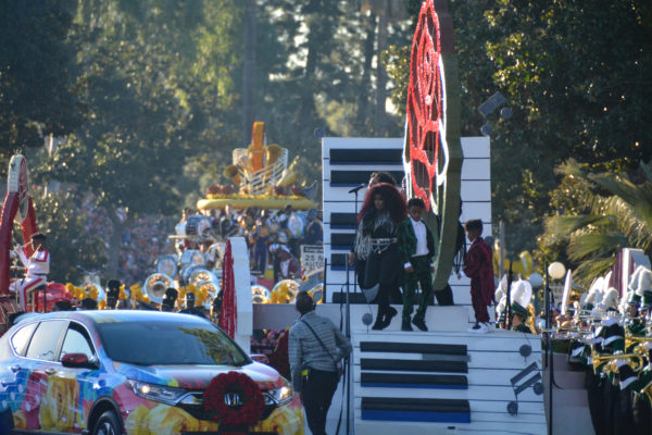 Chaka Khan performs atop float shaped like a winding piano keyboard with a red rose in the center, with her grandsons on either side of her and marching band members on both sides of the float