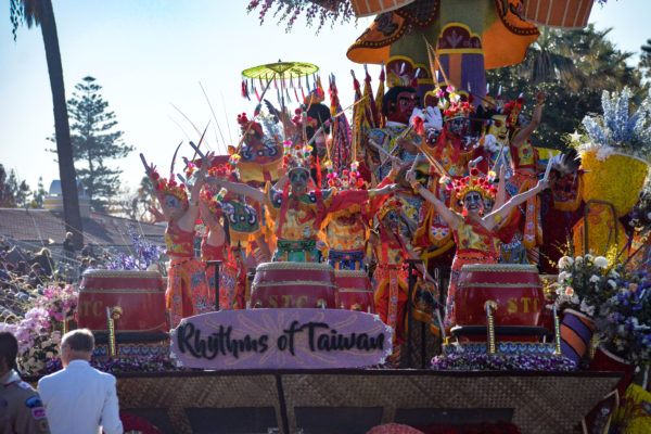 Performers in red Chinese kimonos sing behind float sign, "Rhythms of Taiwan"