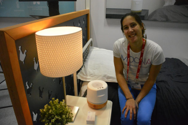 Moona CEO Coline Juin on a "bed" in Eureka Park exhibit with Moona sleep system on the bedside table