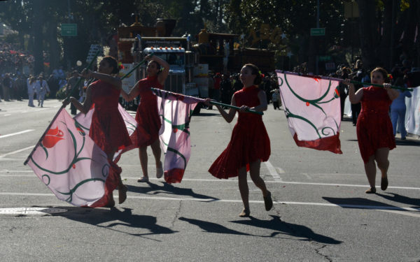 Four female flag carriers dance and swirl white flagss with half-circles on them in front of disabled train float