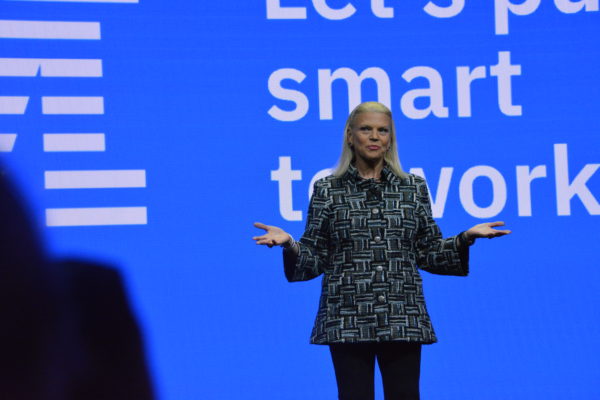 IBM President and Chair Ginni Rometty onstage in front of IBM "Let's Put Smart to Work" slide