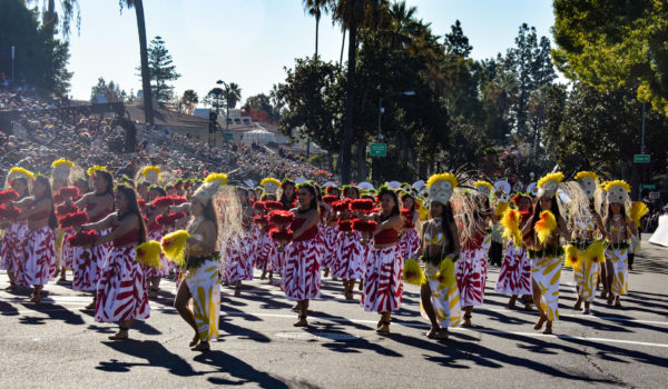 female dancers in grass skirs with yellow and red tops and plumes in their headdresses