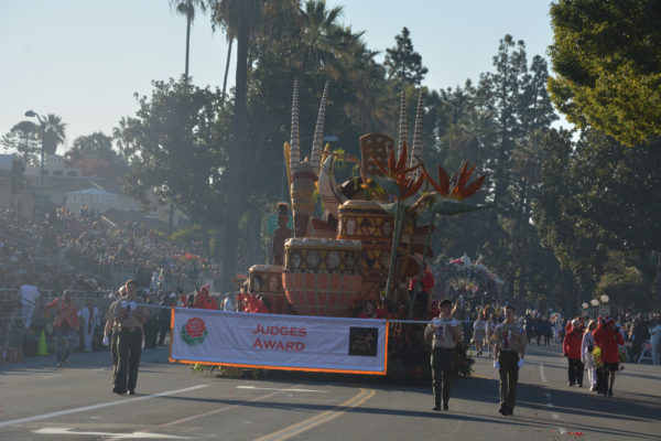 Two Boy Scouts walk with "Judges Award" white banner with red lettering in front of float with two towering African drums at its front