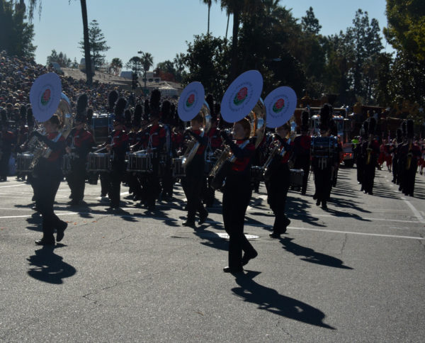 Lincoln Way bandmembers in black slaccks and red jackets, playing tubas with white screens and red Rose Parade rose emblem