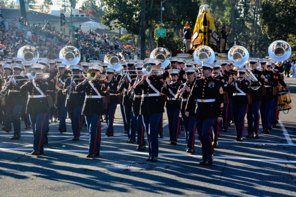 Marines in dress blue uniforms with white belts and hats play trombone and tubas as they march in the Rose Parade