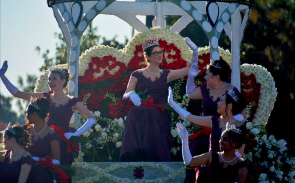 Rose Queen Louise Deser Siskel, surrounded by her court, waves to crowds from red-rose-coverd "throne" of crown-shaped float as she and her princesses wear purple gowns and elbow length white gloves