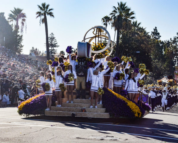 Cheerleaders in white uniforms ride Washingotn float with bit "W" and a football in the center, and surround a Husky costumed mascot