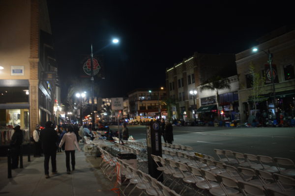 People walk past rows of white chairs on Colorado Boulevard in predawn hours