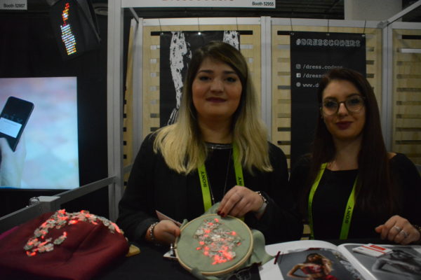 Two young female designers pose with embroidery hoop with needlework interspersed with LED lights