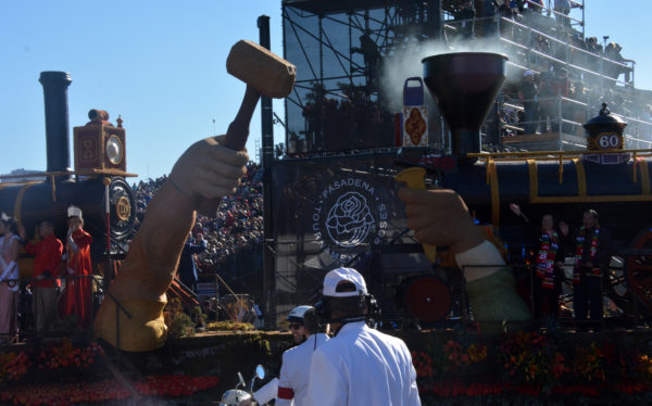 Closeup of hammer and spike on Harmony Through Unity float infront of steam engine as White Suiter and police officer, on motorbike, accompany the float