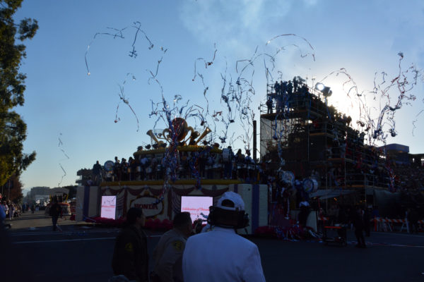 Opening Honda float with rose emblem on top shoots streamers into the air at the start of Rose Parade 2019 as a Whit Suiter and audience watches