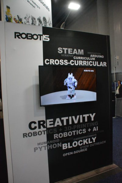 STEAM Robotis sign at CES exhibit features picture of white dancing mini humanoid robot and words STEAM, Creativity, and Cross-Curriculum