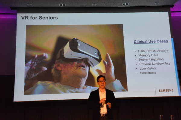 Dr. Rhew with slide that shows elderly woman using a white VR headset at Virtual Medicine conference
