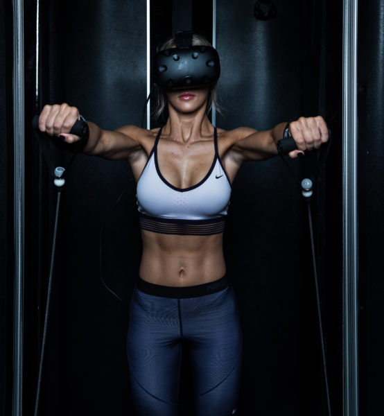 Woman in workout clothes in resistance-traning machine as she wears a VR headset