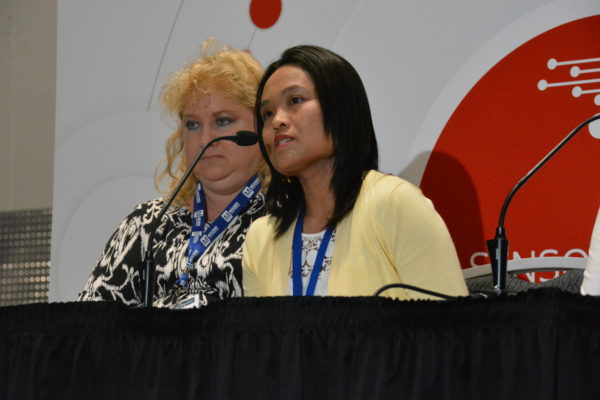 Jocelyn Tan speaks into microphone as Merlena Nickel Johnson listens