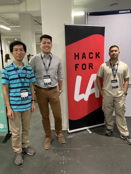 Three team members stand near Hack For LA sign