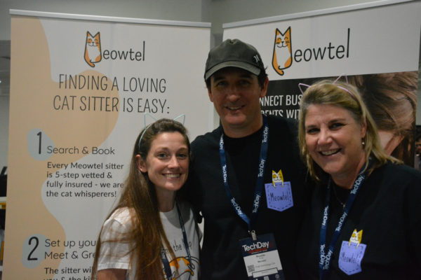 Three staffers of Meowte--a man flanked by two women wearing cat ears--stand before their sign on Tech Day L.A. exhibit floor