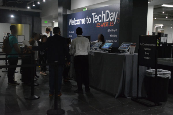 Attendees in suits check in at main desk in front of "Welcome to TechDay" sign