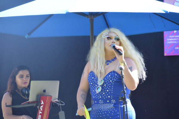 Drag queen Clitdreese on mic with DJ in the background at San Gabriel Valley Pride 2019