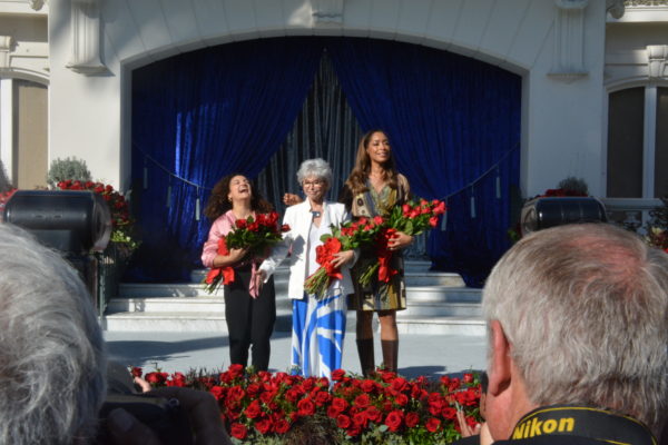 Laurie Hernandez throws her head back laughing as fellow Grand Marshals Rita Moreno and Gina Torres stand nexxt to her and the three regain their bouquets