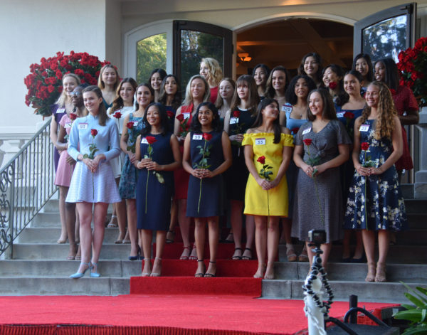 Twenty-five finalists stand on red-carpeted stairs outside Tournament House, flanked by urns filled with red roses