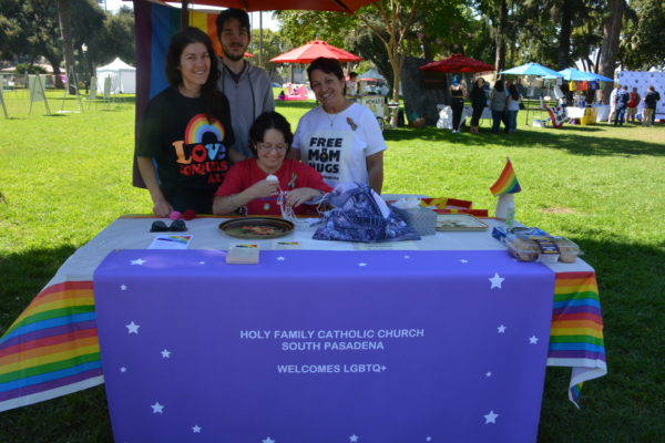 Holy Family Catholic Church staffers sit behind a table with a purple tablecloth at SGV Pride